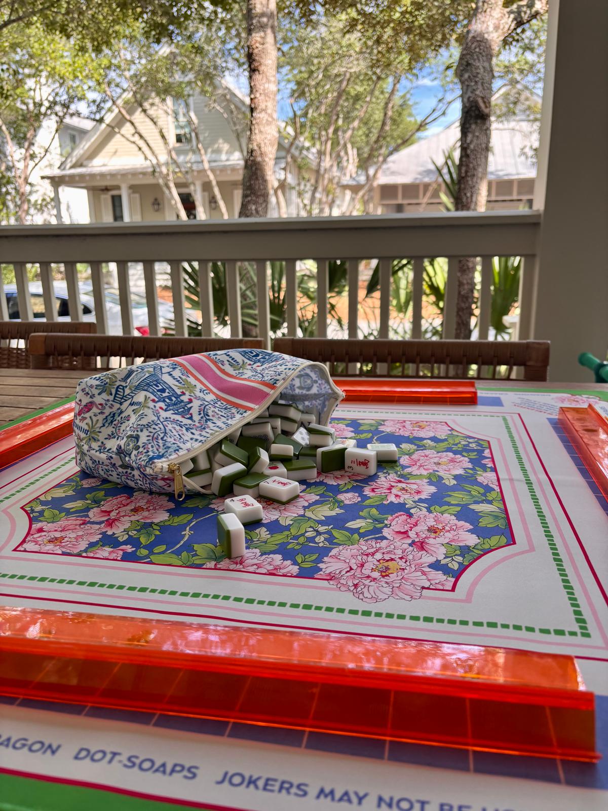 Mahjong tiles arranged on a floral mat on a shaded coastal porch